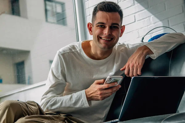 smiling man with mobile phone and computer at home