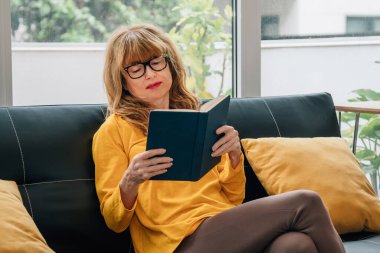 Oturma odasında kitap okuyan bir kadın.