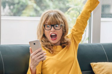 woman with mobile phone at home and expression of success or surprise