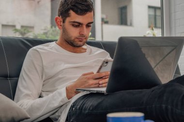 Evde cep telefonu ve bilgisayarı olan genç adam.