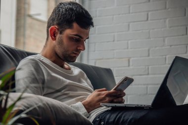 Evde cep telefonu ve bilgisayarı olan genç adam.