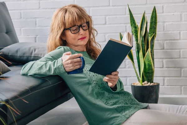 woman at home reading textbook with cup of coffee