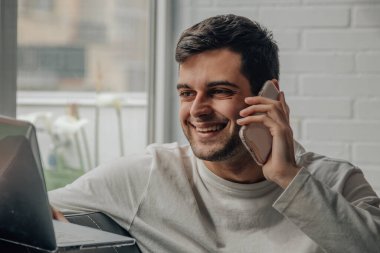 Cep telefonuyla konuşan genç bir adamın portresi. Bilgisayarla çalışıyor.