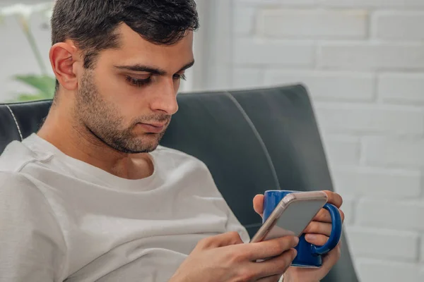 Joven Con Taza Café Casa Mirando Teléfono Móvil —  Fotos de Stock