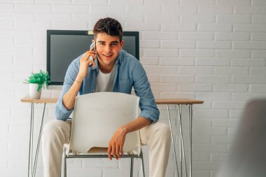 student at home with mobile phone and desk with computer behind