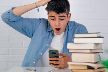 student at the desk with books surprised looking at the mobile phone