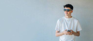 Duvarda cep telefonu ve güneş gözlüğü olan genç bir çocuk izole edilmiş.