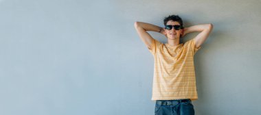 Güneş gözlüklü rahat genç çocuk duvara yaslanıyor.