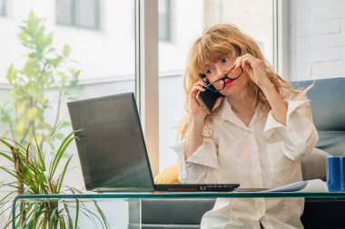 Cep telefonlu bir kadın bilgisayara bakıyor.