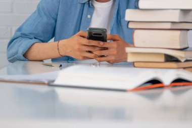 Öğrenci elleri ve cep telefonu masanın üstünde kitaplar.
