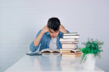 Öğrenci yığınla kitapla masada çalışıyor.