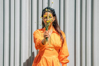 Elinde çiçek demeti ve turuncu elbisesi olan kız.