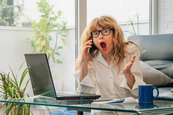 Vrouw Met Mobiele Telefoon Thuis Verrast Zoek Naar Computer — Stockfoto