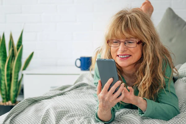 Kobieta Średnim Wieku Telefonem Komórkowym Łóżku — Zdjęcie stockowe