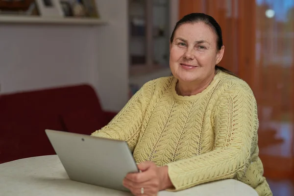 Senior woman in yellow sweater looking in the camera with tablet — Stock Photo, Image