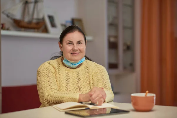 Senior dame i gul genser ser inn i kameraet med maske – stockfoto