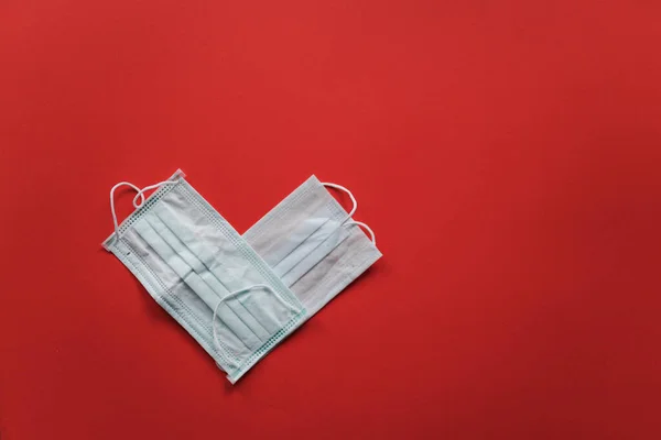Символ сердца сделан из двух медицинских масок на красном фоне. День Святого Валентина во время пандемии коронавируса — стоковое фото