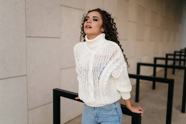 Uma menina de camisola branca e jeans azuis com a cabeça apoiada atrás das mãos em um recado de metal — Fotografia de Stock