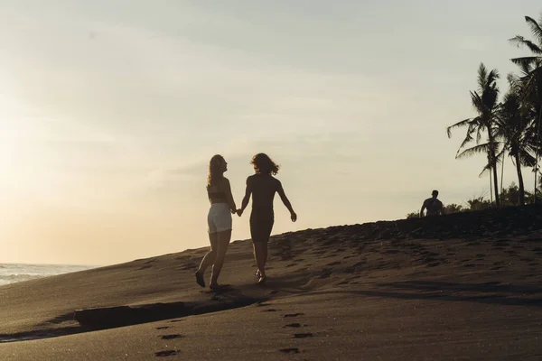 Una giovane coppia di amanti corre su una spiaggia tropicale sullo sfondo di un tramonto e si tiene per mano — Foto Stock