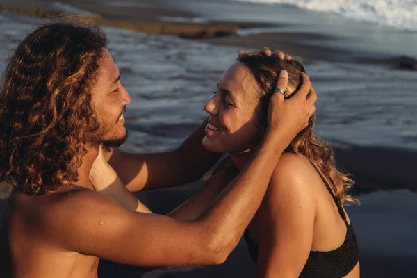 Un couple lumineux amoureux s'admire l'un l'autre l'homme caresse les cheveux des filles et ils se regardent doucement sur le fond de l'océan roulant leurs vagues — Photo