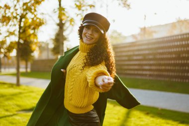 Parlak yeşil dostum sarı bir kazak giydi şık kıvırcık güzellik sarı yapraklar ve sonbahar parkının yeşil çimleriyle mükemmel uyum içinde.