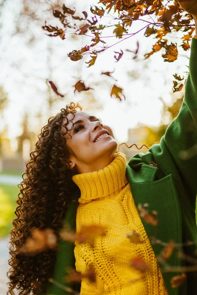 Una ragazza nel parco tira le mani verso le foglie degli alberi. Autunno, umore positivo. — Foto Stock