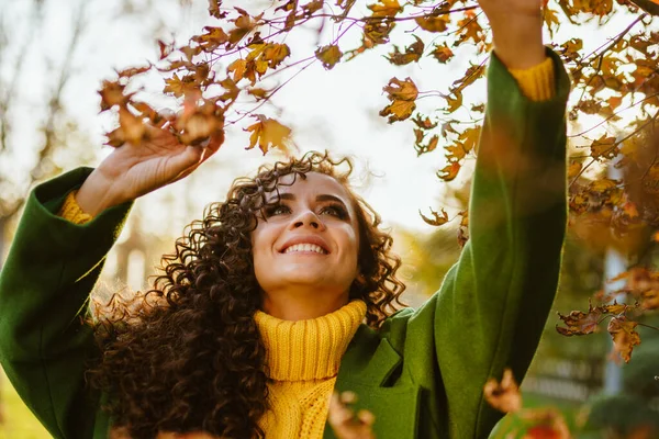 Het meisje speelt met herfstbladeren in het park en glimlacht. — Stockfoto