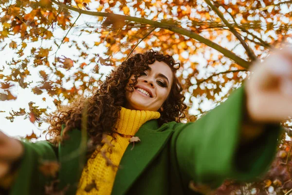 Chica brillante divirtiéndose contra el fondo de los árboles de otoño y extiende sus manos en la cámara. — Foto de Stock
