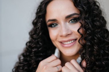 Kıvırcık esmer güzellik gülümser güzel beyaz dişli gülümseme ve el ele tutuşur kapı süveteri