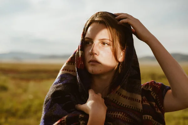 In the steppe, a girl of European appearance with a shawl over her head and shoulders with an oriental coloration looks into the distance — Stock Photo, Image