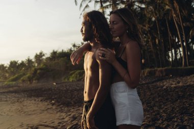 Bali 'nin kara kumsalında birbirine aşık güzel bir çift var. Avrupalı bir kadın, Doğu Asyalı bir adamın çıplak gövdesinin arkasından sarılıyor.