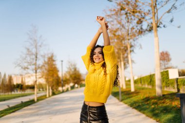 Pistte kafasının üzerinden kaldırırken çapraz eller üzerinde parlak sarı bir kazak giyen kız karnını gösteriyor.