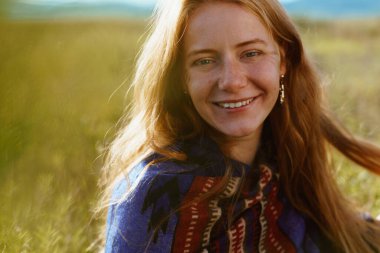 Yüzünde çiller olan kızıl saçlı, neşeli bir gülümseme ile terk edilmiş bozkırda sarı çimenli bir kız.