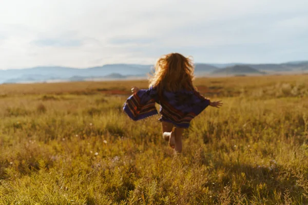 Una chica pelirroja corre al atardecer en un campo contra el telón de fondo de las montañas. Silueta irreconocible — Foto de Stock