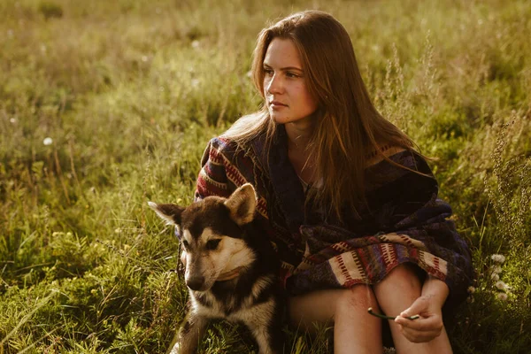 A young girl sits in a field with a dog. Dressed in a poncho, ethnic theme. — Stock Photo, Image