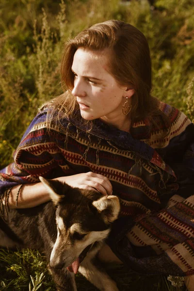 Mysterious portrait of a girl with a dog, dressed in ethnic clothing. Sitting at sunset in a field — Stock Photo, Image