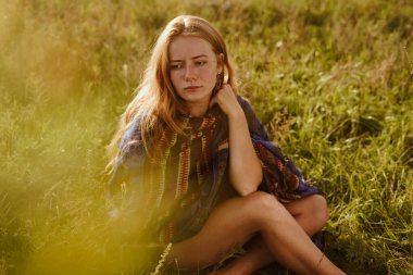 Düşünceli bir bakış, üzgün bir şekilde kapalı dudaklar ve makyajsız kızıl saçlı bir güzelin yüzünde hafifçe yer değiştiren kaşlar omuzlarında etno bir pelerin ile güzel, güçlü ve ince olanı kapatmıyor.