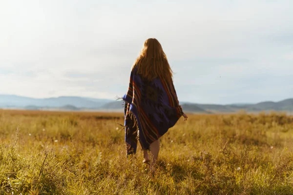 En la hierba de la estepa en la distancia hacia las colinas va chica descalza en una capa larga con el pelo rojo largo — Foto de Stock