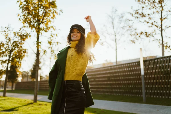 Een mooi meisje gekleed in de stijl van een molenachtige golven naar iemand met haar hand die de aandacht trekt tegen de achtergrond van de muur in het herfstpark — Stockfoto