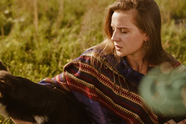 Girl in Indian national cape without makeup with long red hair strokes dog sitting on steppe grass — Stock Photo, Image