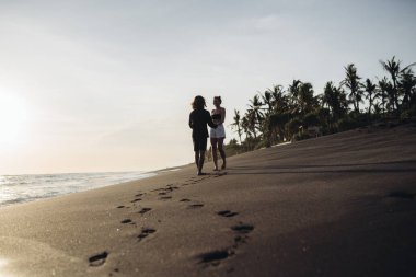 Sahildeki karanlık kumda bir adam ve bir kadın duruyor ve okyanusa bakıyor.