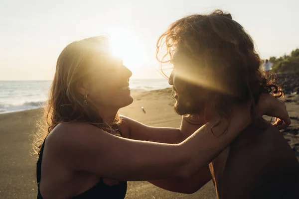 Homme et femme se regardant dans l'amour dans les rayons du soleil couchant sur le fond du sable et des eaux de l'océan — Photo