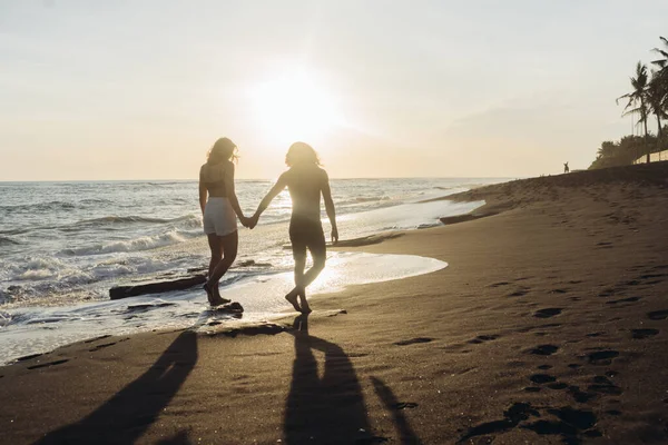 Uomo e donna vagano attraverso l'oceano su acqua e sabbia tenendosi per mano — Foto Stock