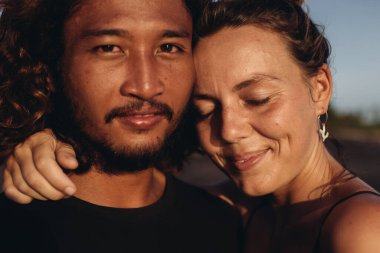 Bir kadın gözlerini kapar ve gülümseyerek Doğu Asyalı bir adamın boynuna sarılır.