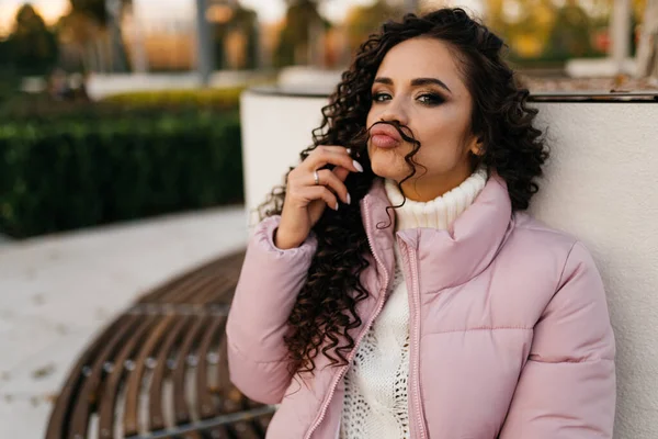 Menina em um banco no parque tolos em torno de aplicar cachos na forma de um bigode para o rosto — Fotografia de Stock