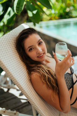 Yakın plan. Sıcak bir günde elinde bardakla havuz kenarında uzanan kız.