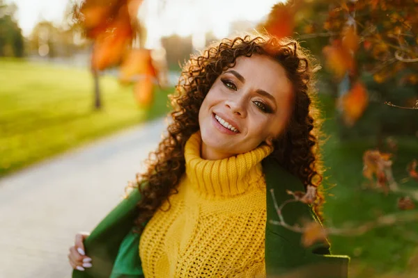 Parque de otoño con follaje carmesí y en la pista en un brillante vestido de otoño de buen carácter sonrisas morena rizada — Foto de Stock