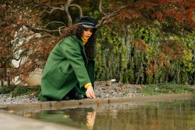 Paltolu kız parktaki su birikintisine çömeldi ve suya uzandı.