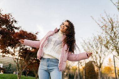 Sıcak sonbahar kıyafetleri içinde bir kız sonbahar parkında dans eder ve poz verir.