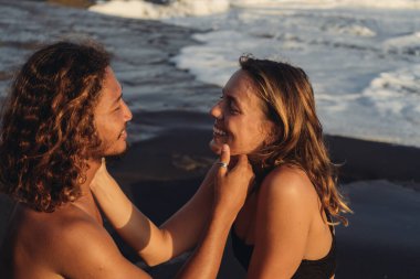 Okyanusun arka planında kara kumları aşıkları birbirlerine bakar ve elleriyle yüzlerine dokunurlar.